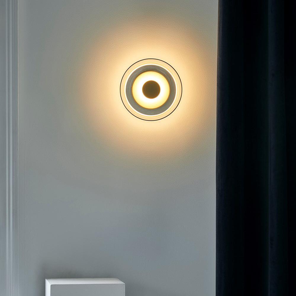Mounted beside a dark curtain on a grey wall, this Clérachic wall light shows a warm halo and a ring of light around its dome.
