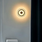 Mounted beside a dark curtain on a grey wall, this Clérachic wall light shows a warm halo and a ring of light around its dome.