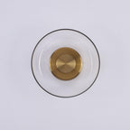 Front view of this Clérachic wall light switched off, with a thin dark glass rim, clear glass and a brushed brass disc.