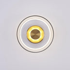 Lit front view of this Clérachic wall light, with a bright ring of light under the clear glass and a glowing brass disc.