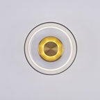 This Clérachic wall light with a clear glass dome, lit, shows a soft white ring and a glowing gold centre on a pale grey wall.