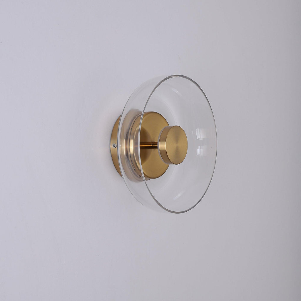 Side view of this Clérachic wall light switched off, with a clear glass dome, a brass stem and a round brass wall plate.