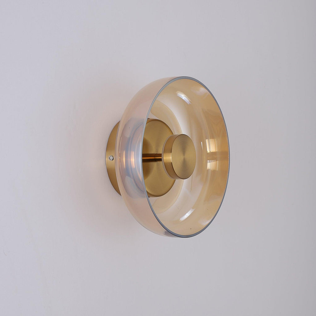 An amber glass dome on this Clérachic wall light, seen from the side with a brass stem, a brass knob and a round back plate.
