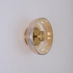 An amber glass dome on this Clérachic wall light, seen from the side with a brass stem, a brass knob and a round back plate.