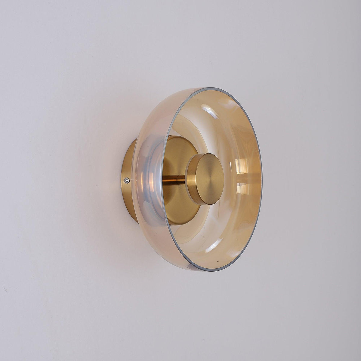 An amber glass dome on this Clérachic wall light, seen from the side with a brass stem, a brass knob and a round back plate.