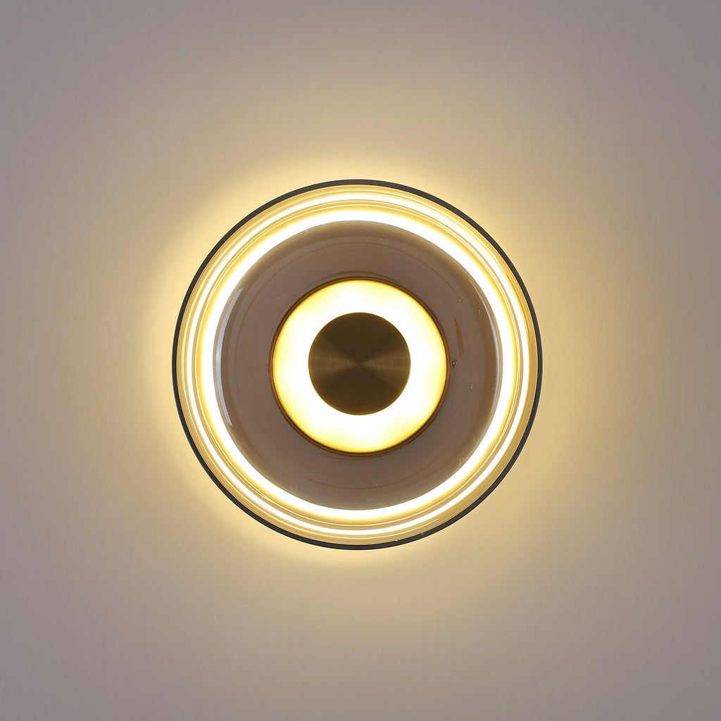 Lit against a grey wall, this Clérachic wall light shows a soft halo, a smoky glass ring and a brass centre disc.