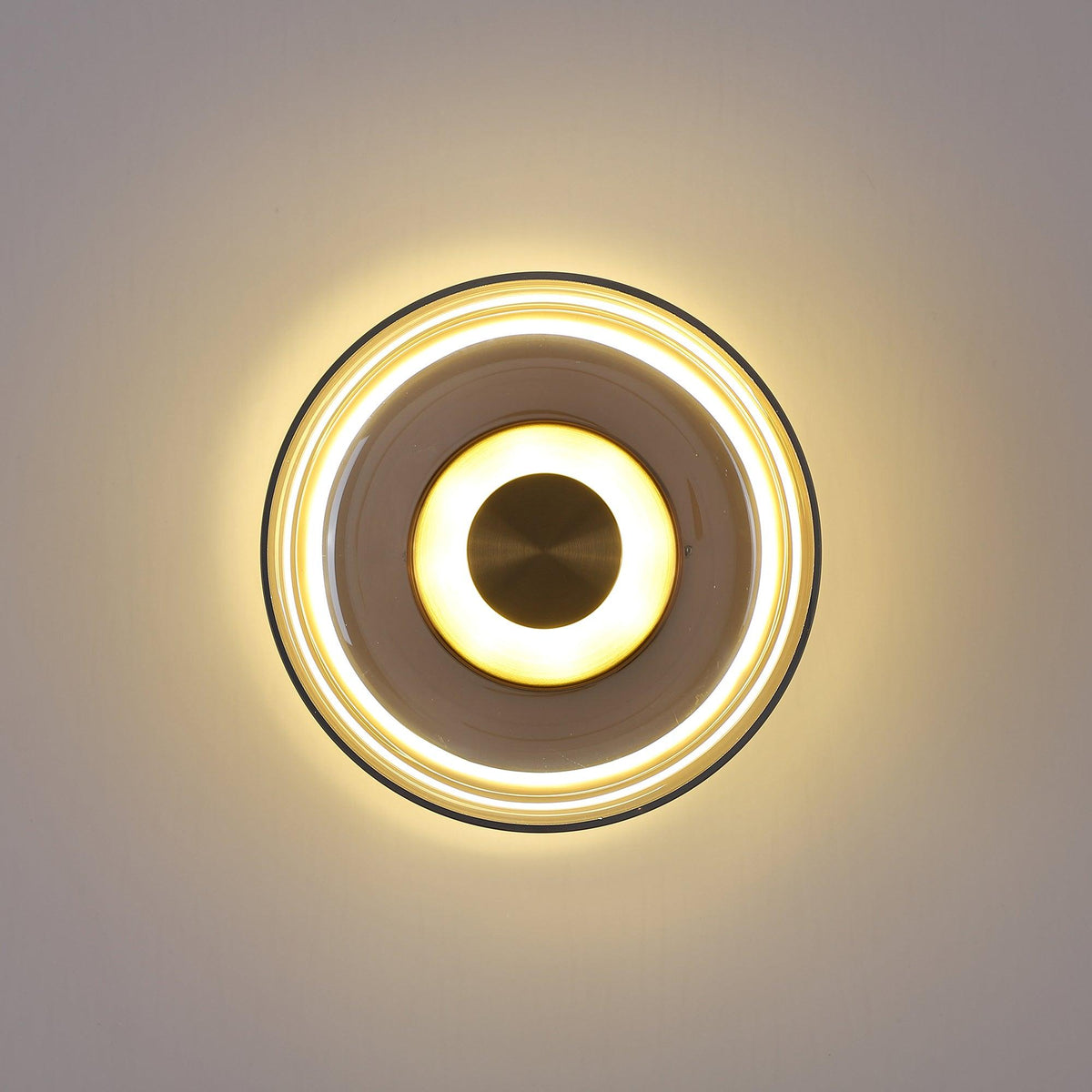 Lit against a grey wall, this Clérachic wall light shows a soft halo, a smoky glass ring and a brass centre disc.