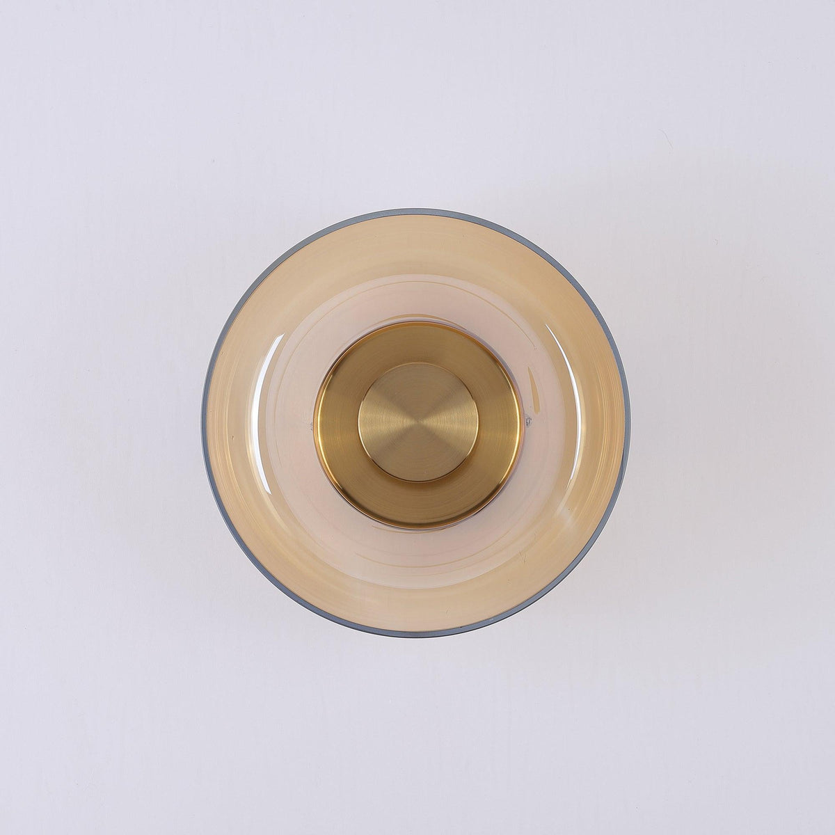 Front view of an amber glass version of this Clérachic wall light, unlit, with a brass disc at the centre of the dome.