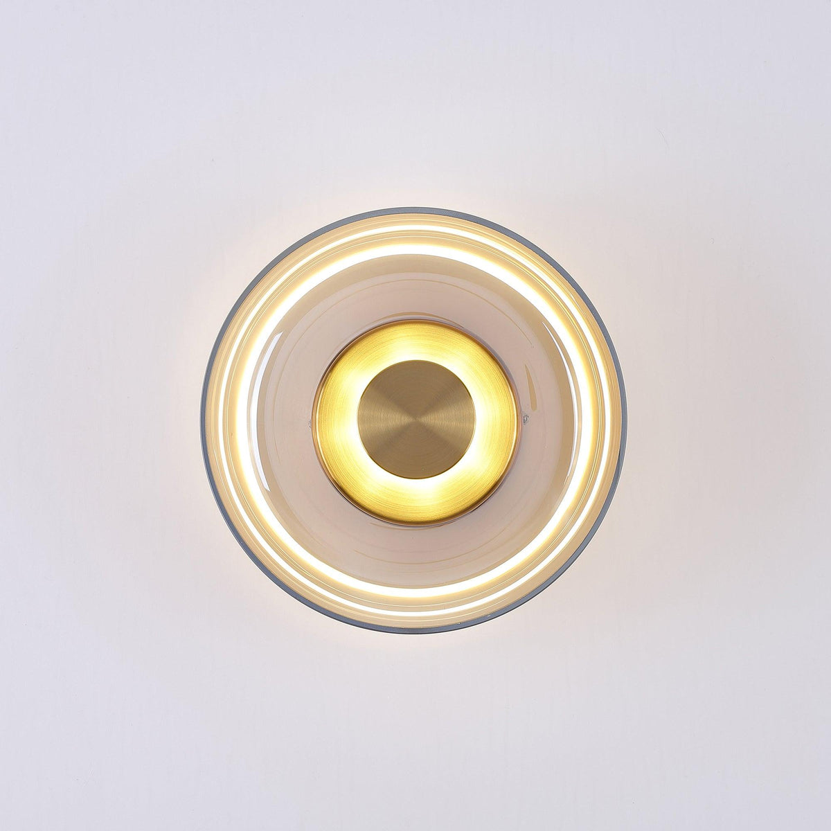 Lit front view of an amber glass Clérachic wall light, with a bright glowing ring beneath the glass and a brass centre disc.