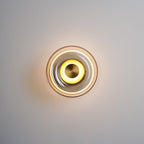 A Clérachic wall light glowing on a grey wall, with a warm centre ring and a clear glass dome edged in a thin dark rim.