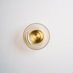 This Clérachic wall light has a pale amber glass dome and a polished brass centre disc, shown unlit on a light wall.