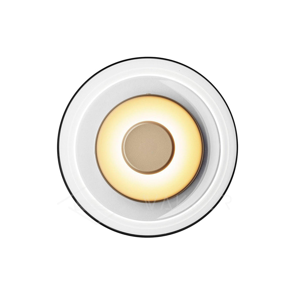 Front view of this Clérachic wall light on white, with a black-rimmed glass dome, a warm glowing ring and a brass centre disc.