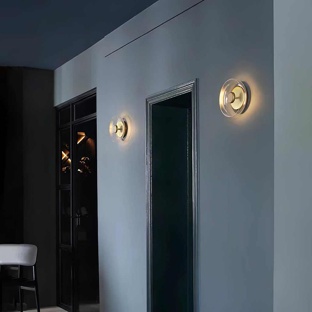 Two Clérachic wall lights glow either side of a dark doorway on a blue-grey wall, one with a clear dome and one with amber.