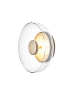 This Clérachic wall light, shown on white with a clear glass dome, has a brass disc held on a short stem.