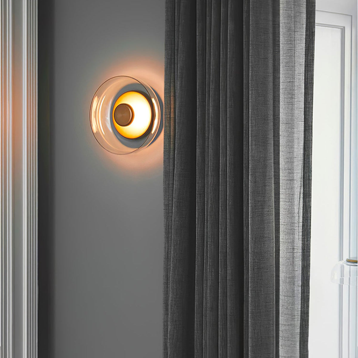 Beside a grey curtain on a charcoal wall, this Clérachic wall light glows orange through its glass dome.
