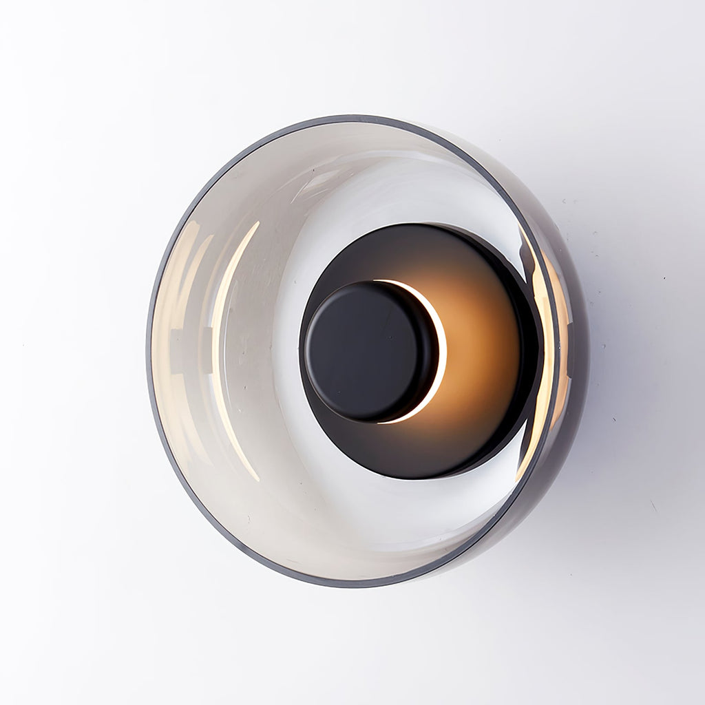 A black-bodied Clérachic wall light with a smoky grey glass dome, showing a crescent of warm light around the black disc.