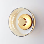 Close view of an amber glass Clérachic wall light with a brass disc, seen at an angle on a white wall.