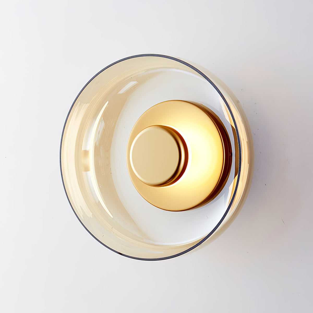 Close view of an amber glass Clérachic wall light with a brass disc, seen at an angle on a white wall.