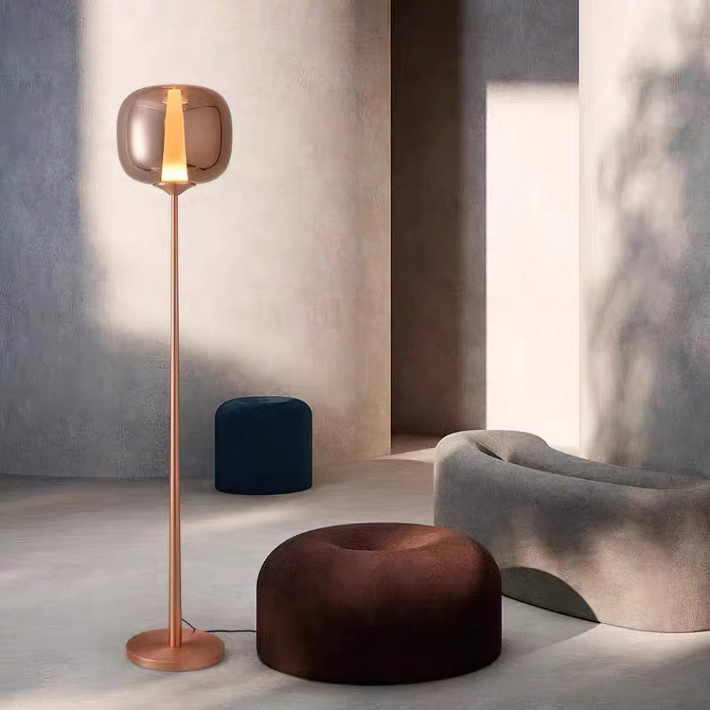 Beside a dark brown round pouf and a grey curved sofa, this rose gold Clérachic floor lamp lights a quiet corner.