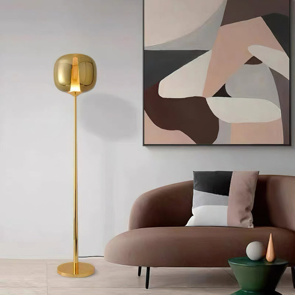 A gold Clérachic floor lamp stands beside a rose-brown curved sofa, with an abstract wall painting in muted tones behind.