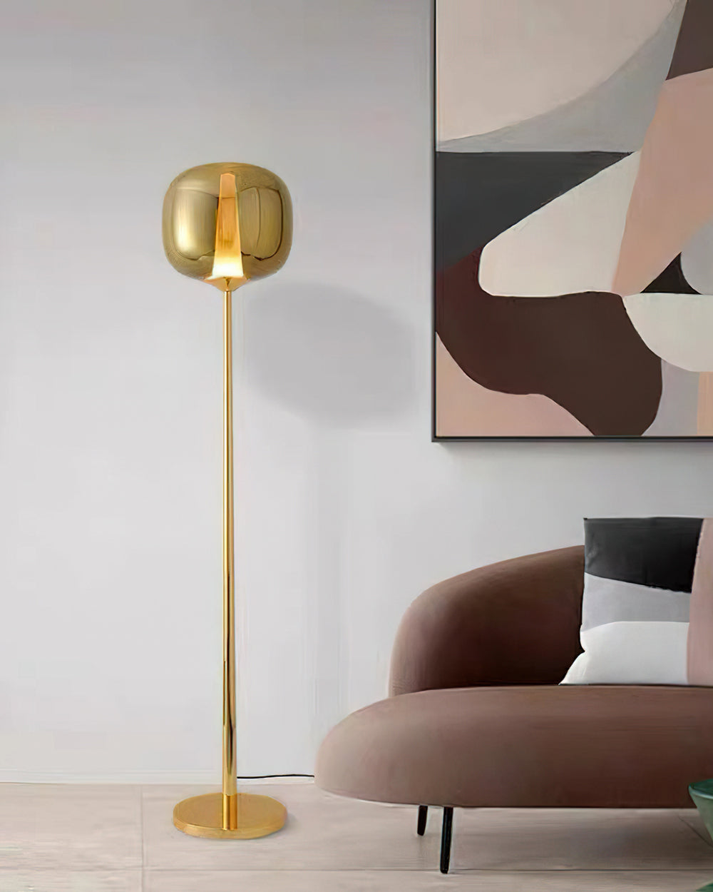 Gold Clérachic floor lamp with a gilt-toned glass head and slim stem, in front of a muted abstract painting and a sofa.