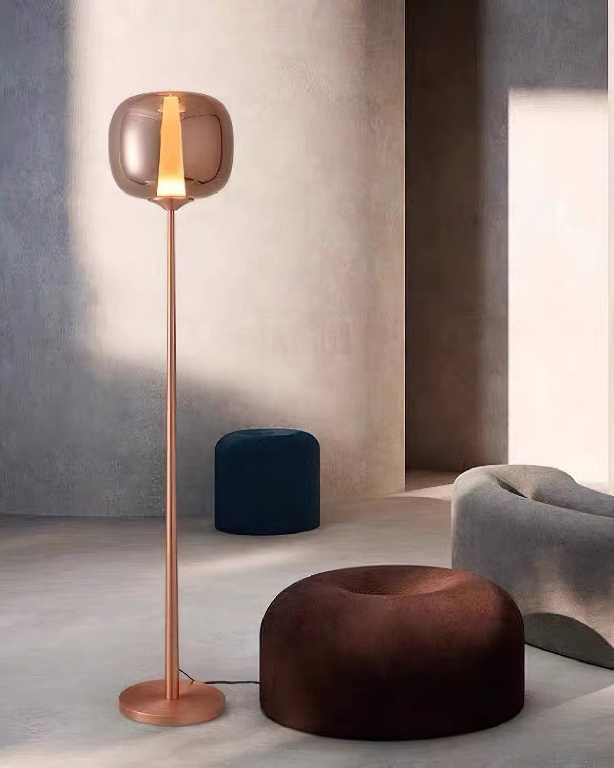 Rose gold Clérachic floor lamp in a quiet room, with a navy pouf and a dark brown pouf at its foot.