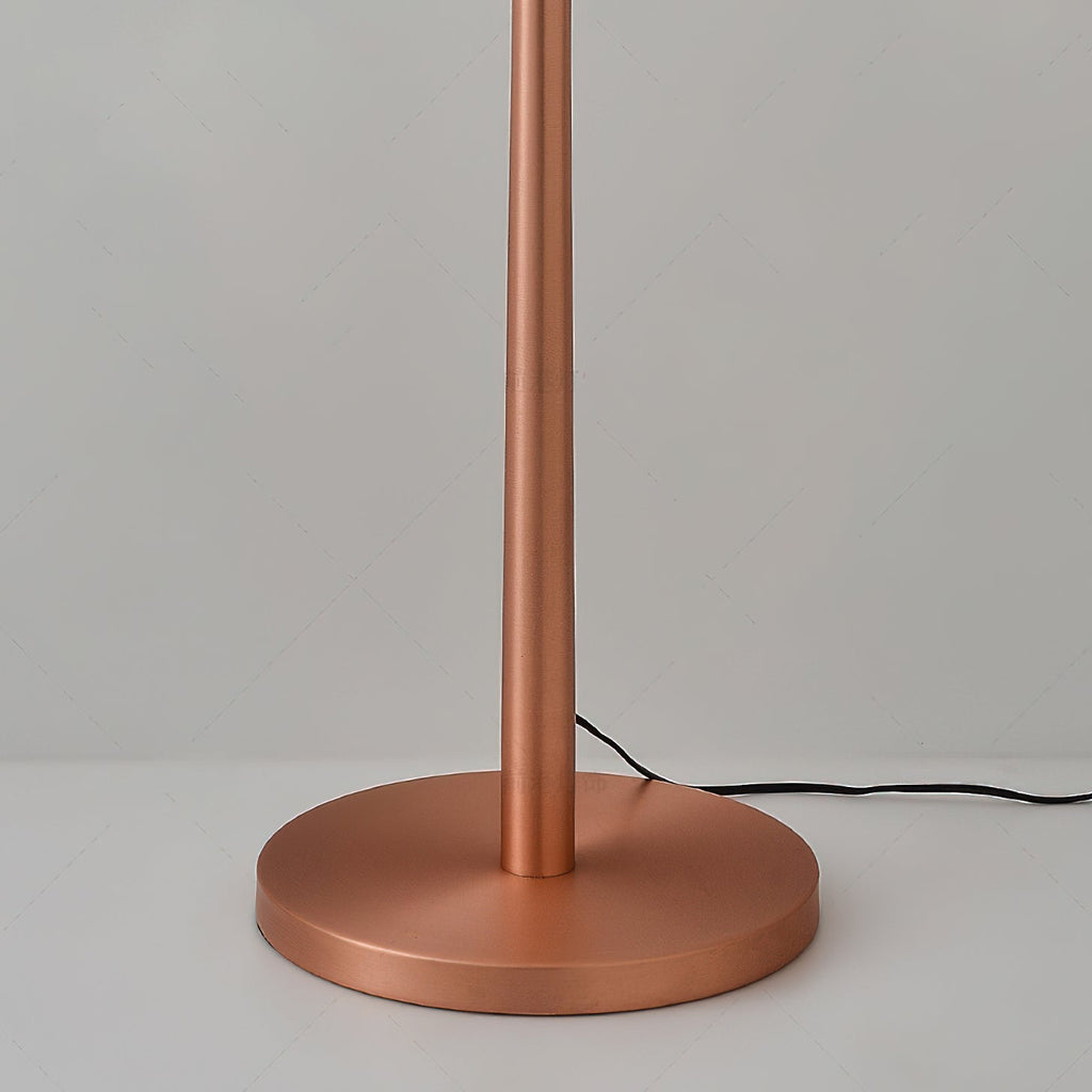 Close view of the weighted round base and the slim rose gold stem of this Clérachic floor lamp, with its cord trailing off.