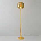Unlit gold Clérachic floor lamp with a gilt glass head on a polished round base, against a pale grey wall.