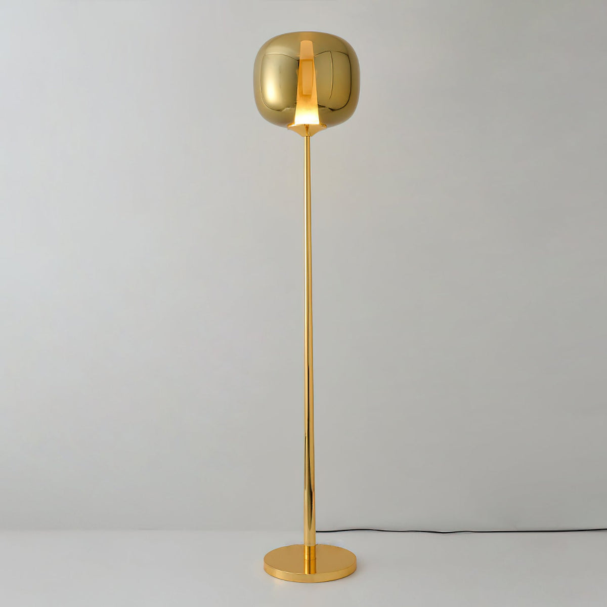 Unlit gold Clérachic floor lamp with a gilt glass head on a polished round base, against a pale grey wall.