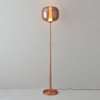 Lit rose gold Clérachic floor lamp with a glowing strip of warm light in its glass head, against a pale grey wall.