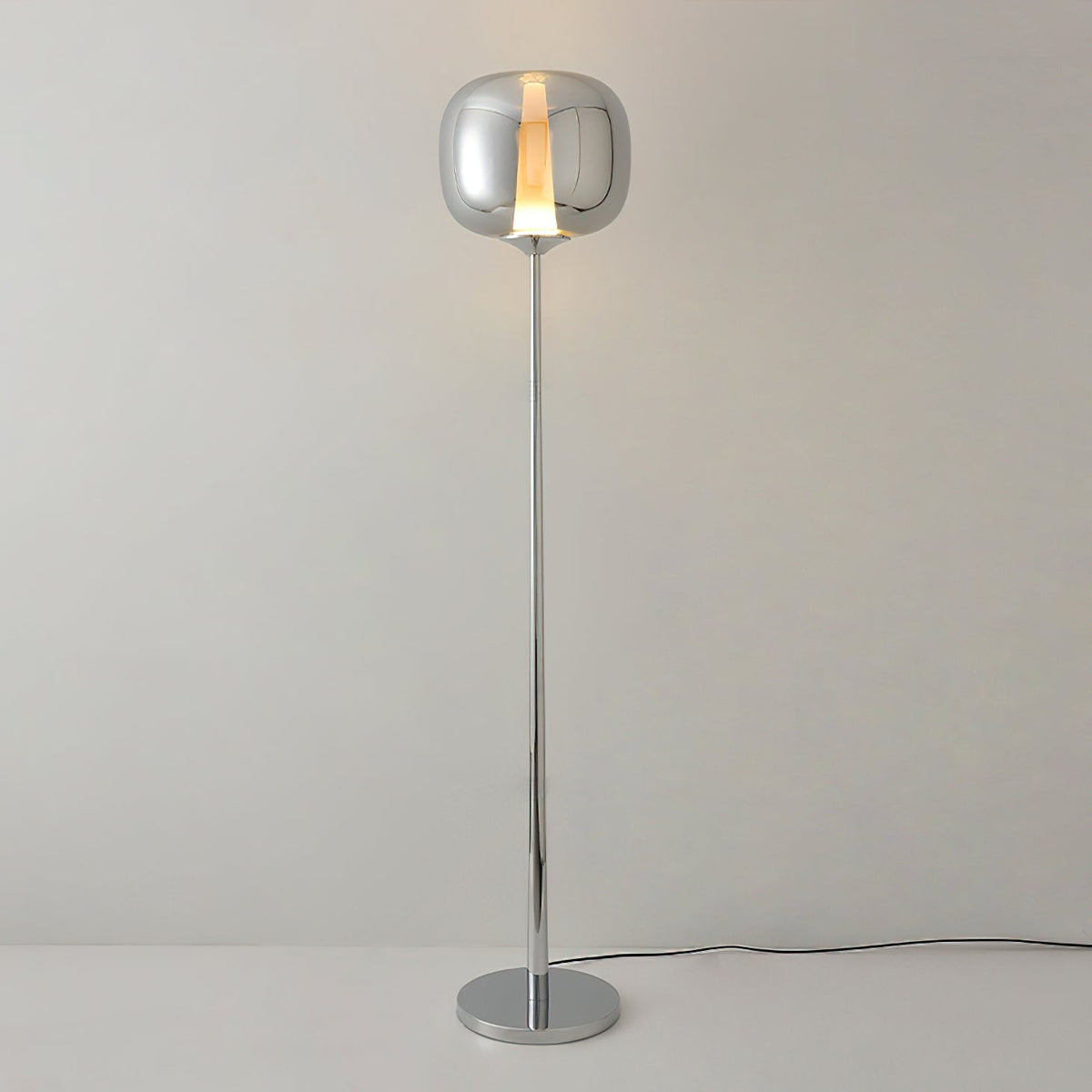 Chrome Clérachic floor lamp with a lit smoked glass head and a polished round base, on a pale grey wall.