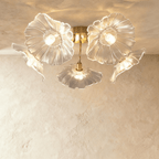 Clérachic five-head ceiling light with clear ribbed glass flower shades on curved brass arms, lit warm against plaster.