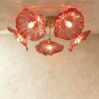 Clérachic five-head ceiling light with red ribbed glass flower shades glowing warm on curved brass arms.