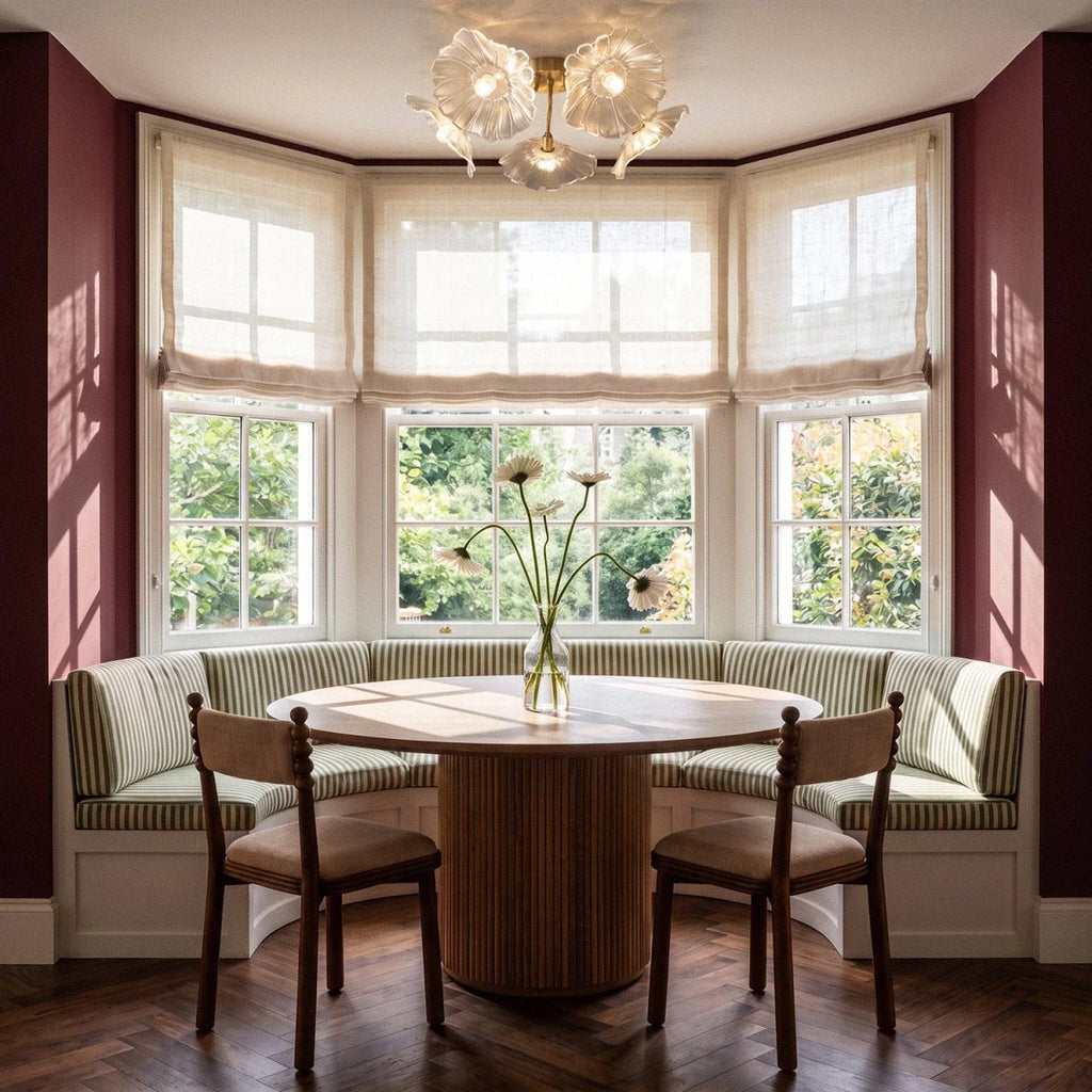Clérachic clear glass flower ceiling light over a round fluted dining table in a bay window with linen blinds.