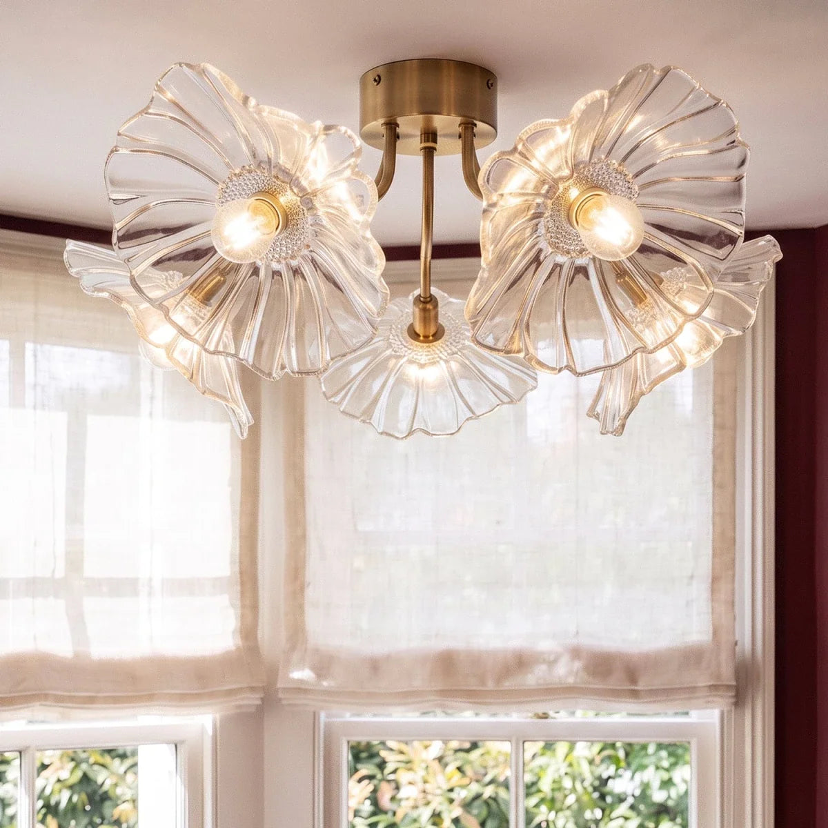 Clérachic five-head ceiling light in clear ribbed glass with a brass canopy, bulbs lit warm beside a sunlit linen blind.