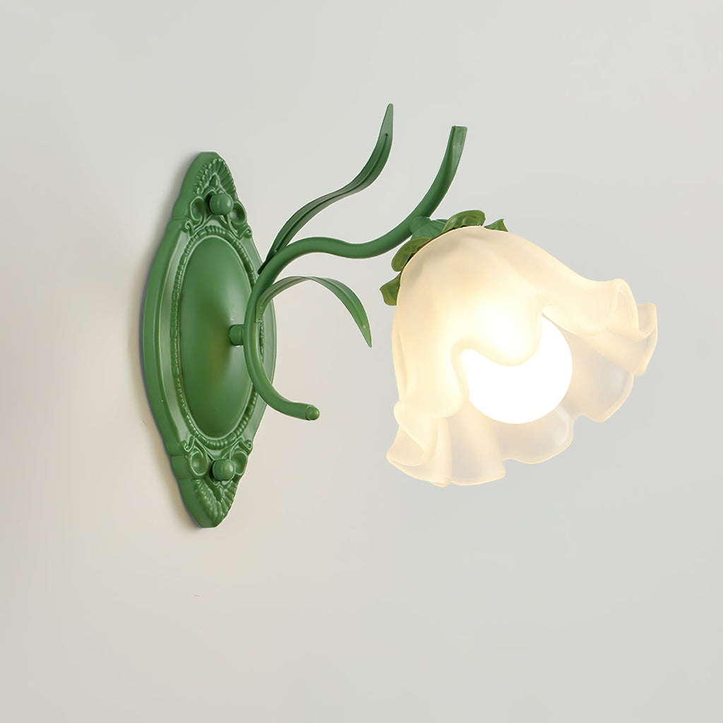 Close, angled view of a green Clérachic wall light with a ruffled frosted glass bloom and a carved oval backplate.