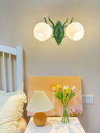 A Clérachic double wall light with two rounded opal glass shades and a green backplate, above a bedside table with tulips.