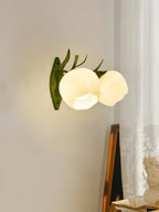 Two rounded glass shades of this Clérachic wall light glow beside a white lace curtain, on a green branch-style arm.