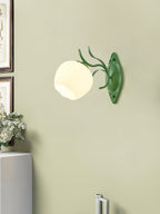 A green Clérachic wall light with a rounded white glass shade, mounted on a pale olive-green wall.