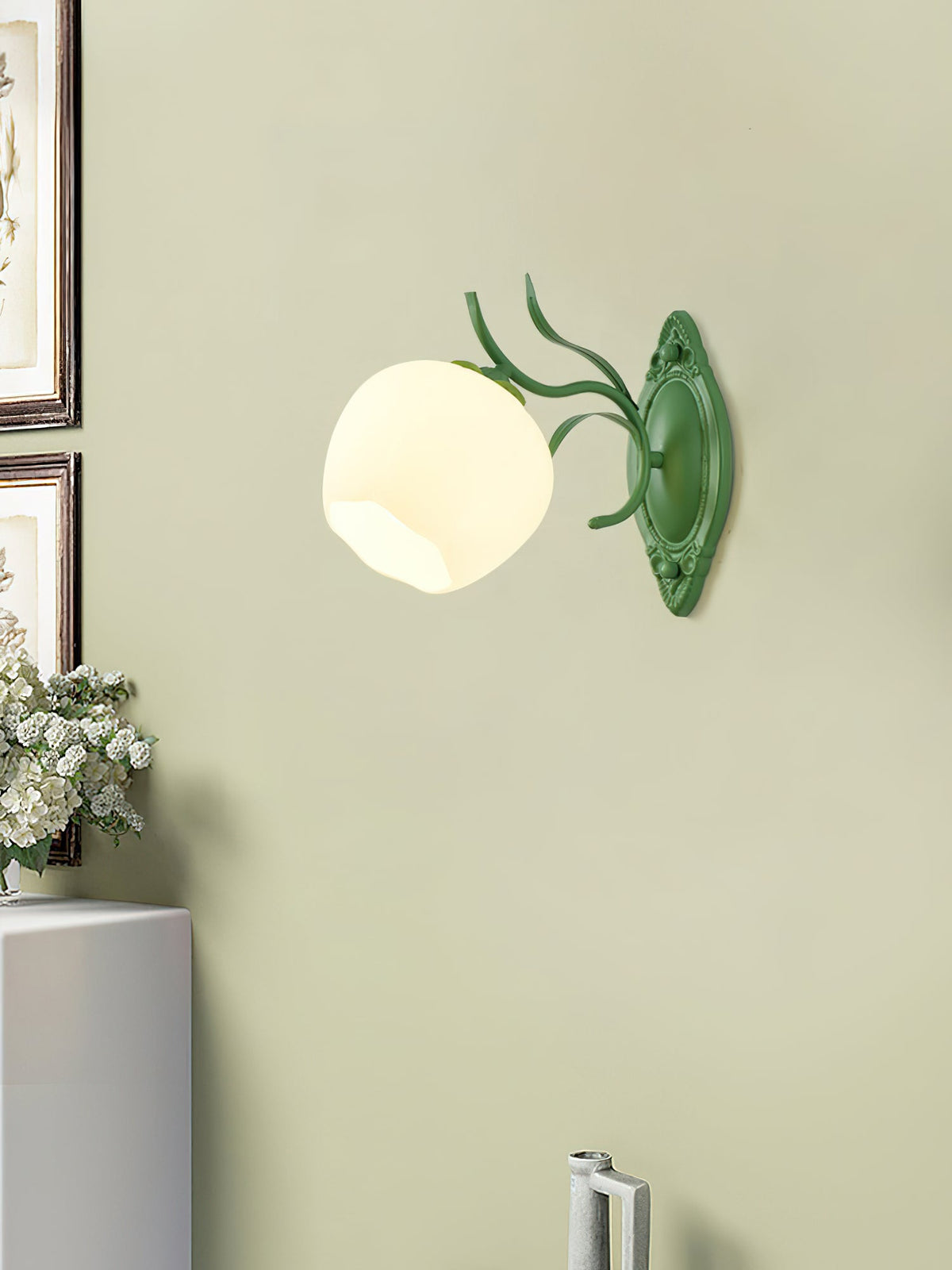 A green Clérachic wall light with a rounded white glass shade, mounted on a pale olive-green wall.