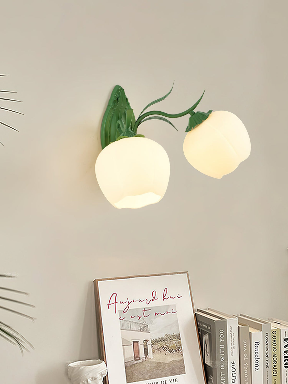 Two opal glass shades on a green Clérachic double wall light, hung above a shelf with books and a framed print.