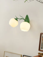 A Clérachic double wall light in green with two soft round glass shades, on a beige wall near a framed picture.