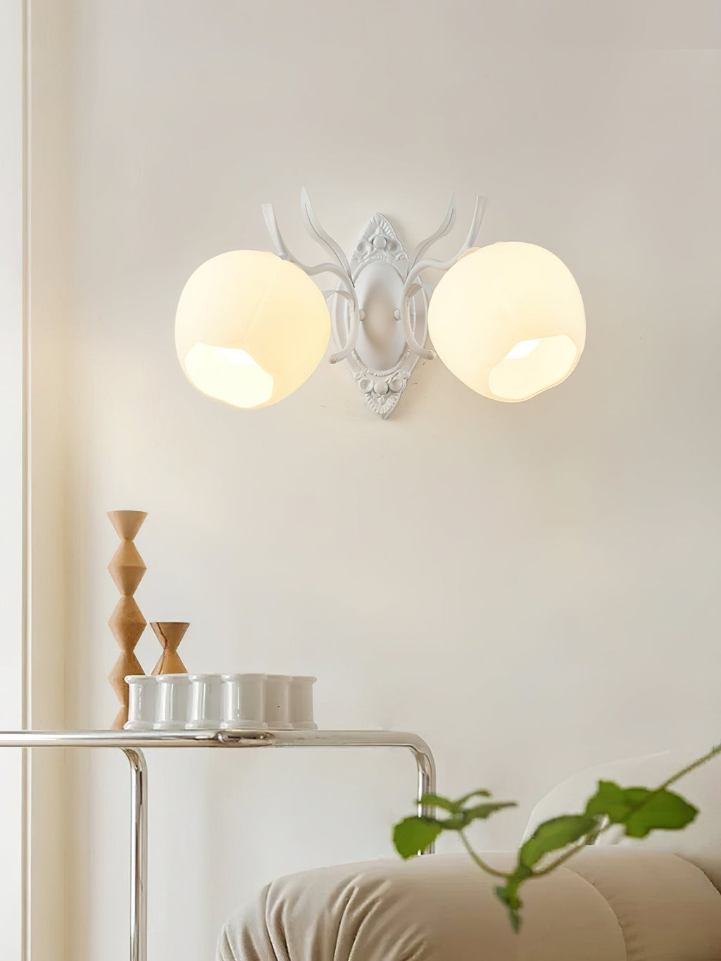 A white Clérachic double wall light with two rounded opal shades and antler-style arms, above a small side table.