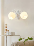 A white Clérachic double wall light with two rounded opal shades and antler-style arms, above a small side table.