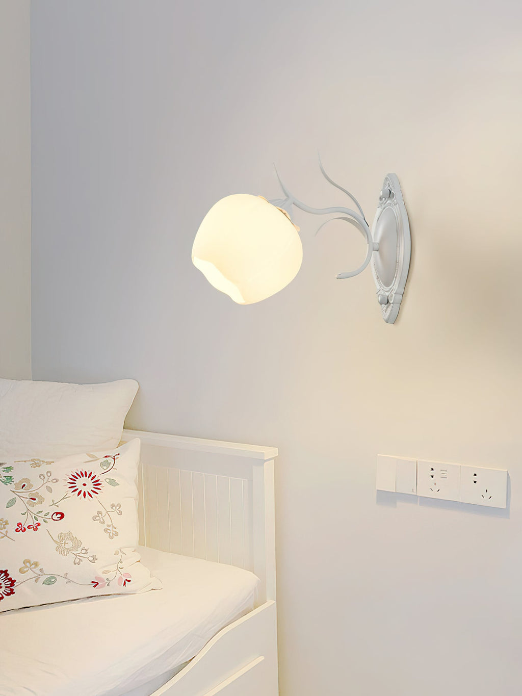 Single white Clérachic wall light with a rounded glass shade on a pale grey wall above a white daybed.