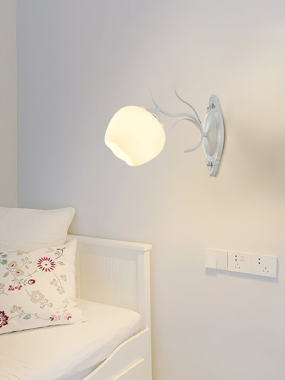 Single white Clérachic wall light with a rounded glass shade on a pale grey wall above a white daybed.