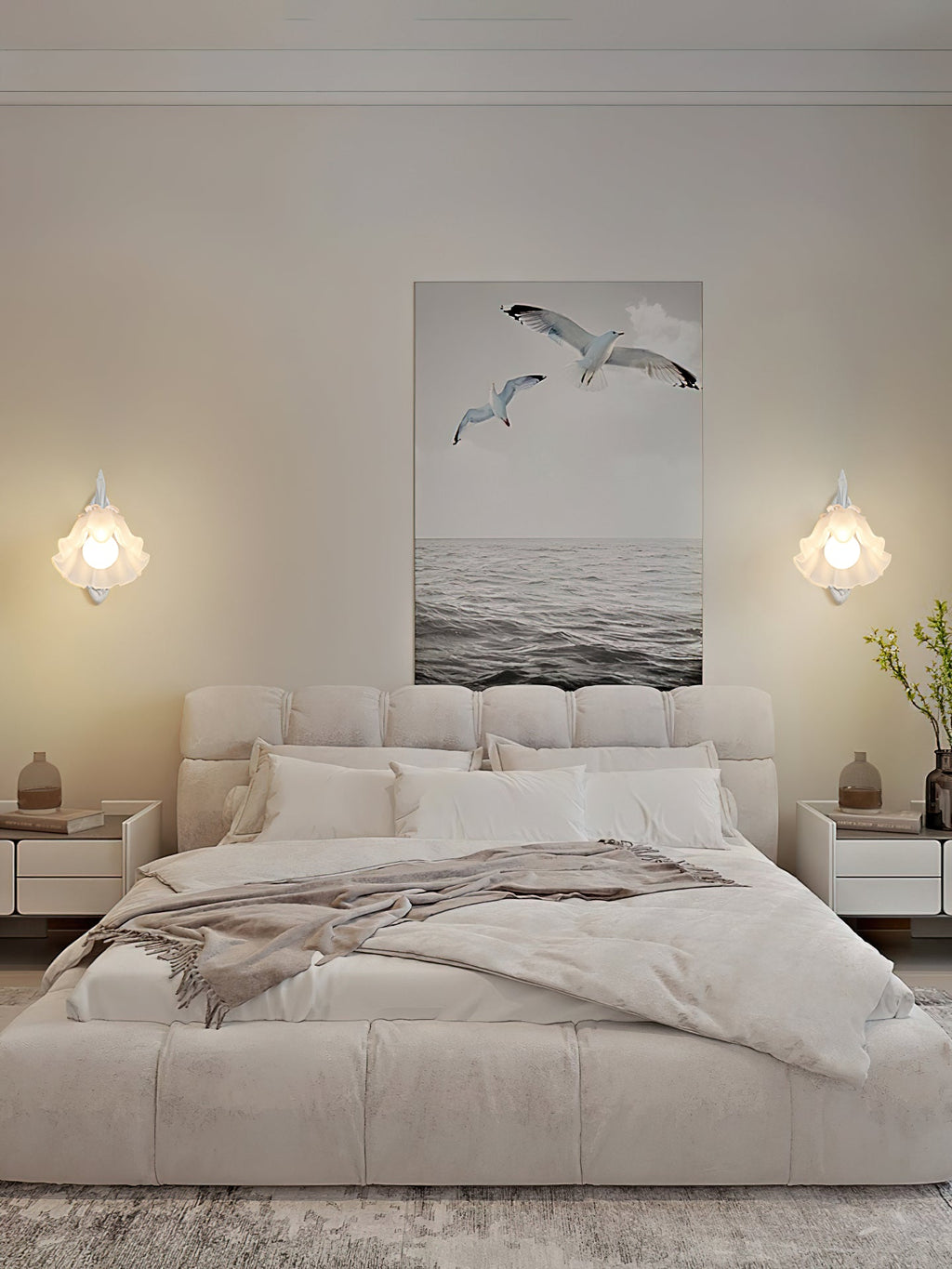 Two small white Clérachic wall lights hang on either side of a seabird print above an upholstered cream bed.