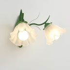 Lit green Clérachic double wall light seen at an angle, with two frosted flower shades and bare bulbs, on a grey wall.