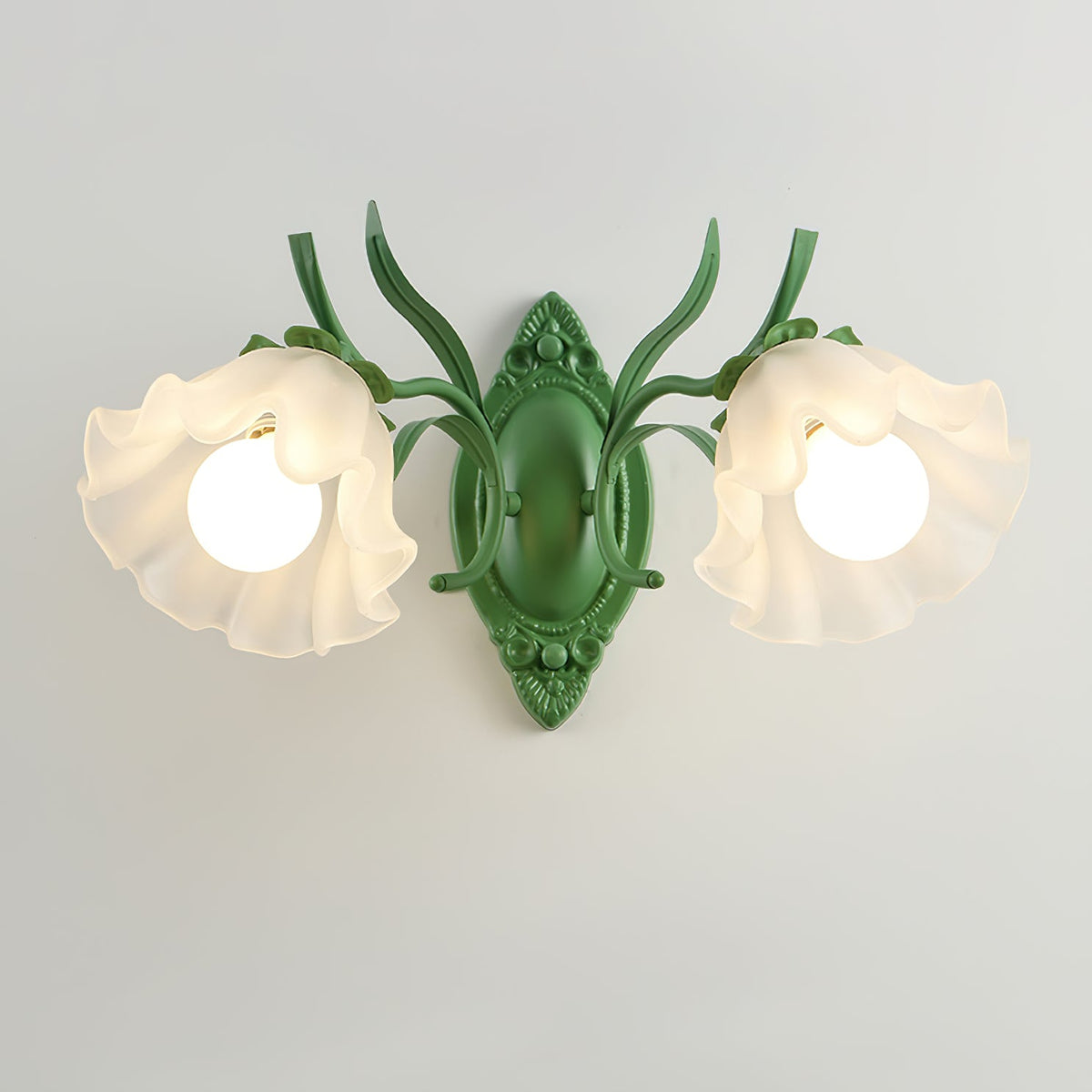 Front view of a lit green Clérachic double wall light, its two frilled frosted shades glowing on a pale grey wall.