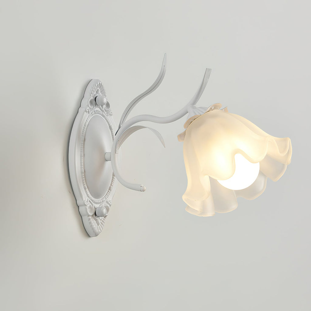 A white Clérachic wall light seen from the side, with a long carved backplate and one frosted flower shade, on grey.